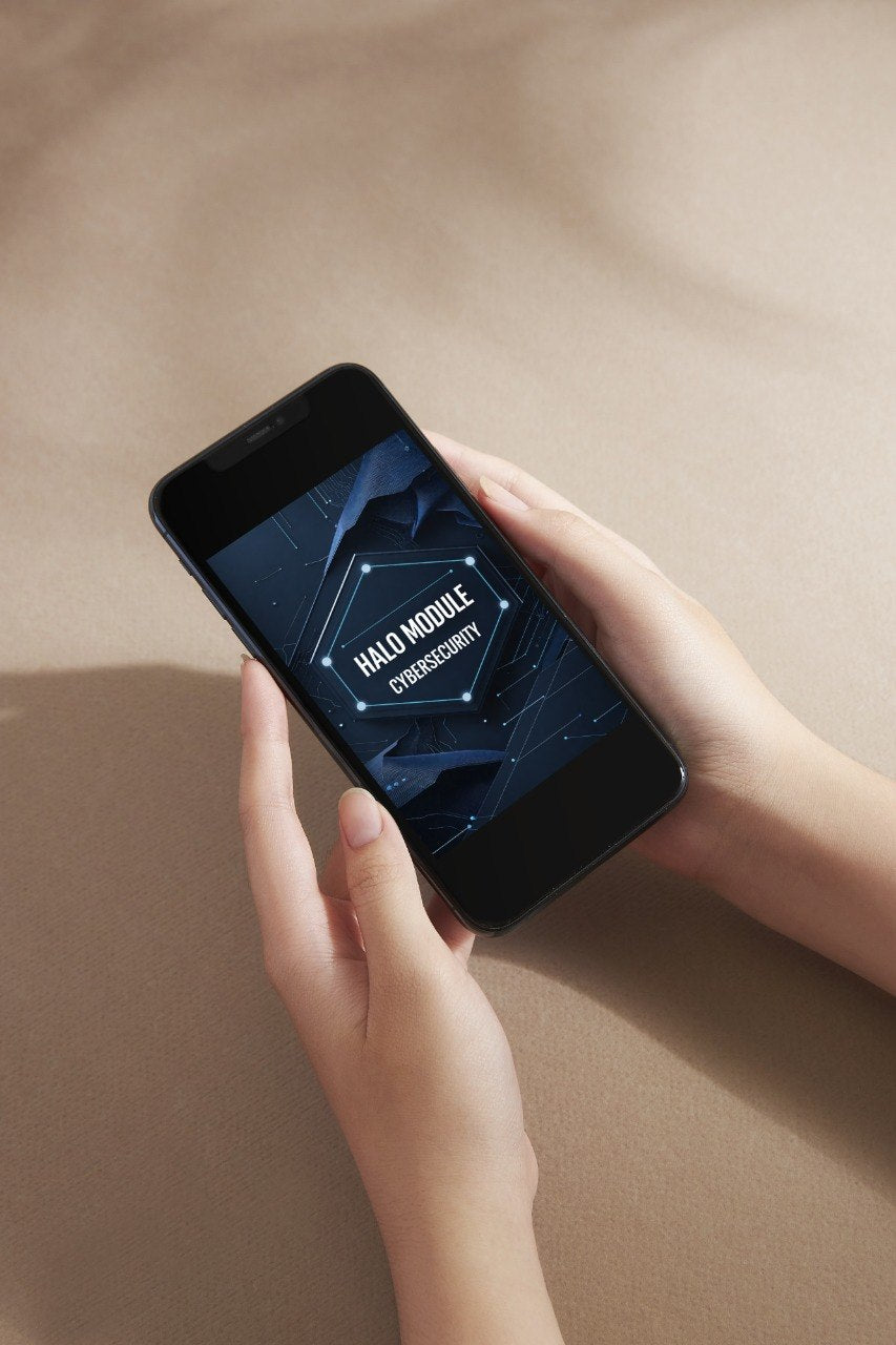 A person holds a black smartphone showing a dark blue digital screen with the text 'HALO MOBILE COMMANDER' against a warm beige background.